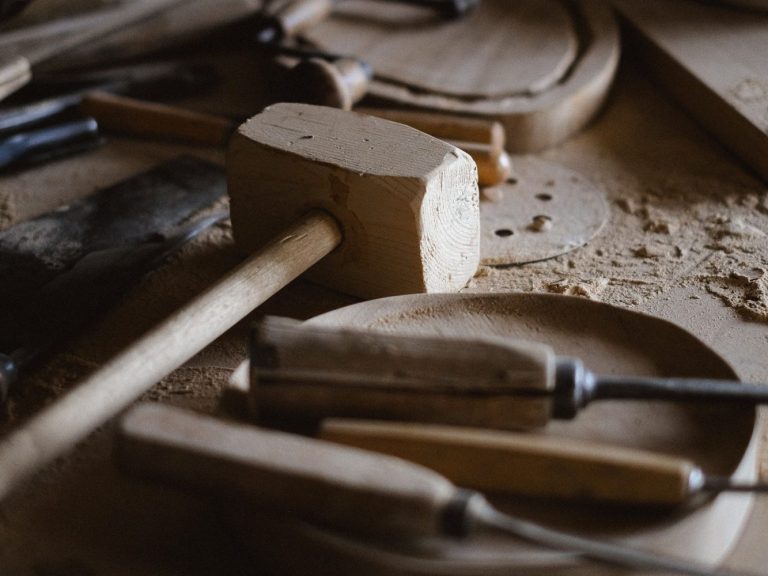 Holzwerkzeuge und -materialien auf einer Werkbank, darunter ein Holzhammer und Schnitzwerkzeuge.